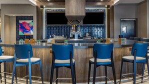 Un área de bar moderna con una barra central, taburetes azules y una gran obra de arte abstracta en la pared.
