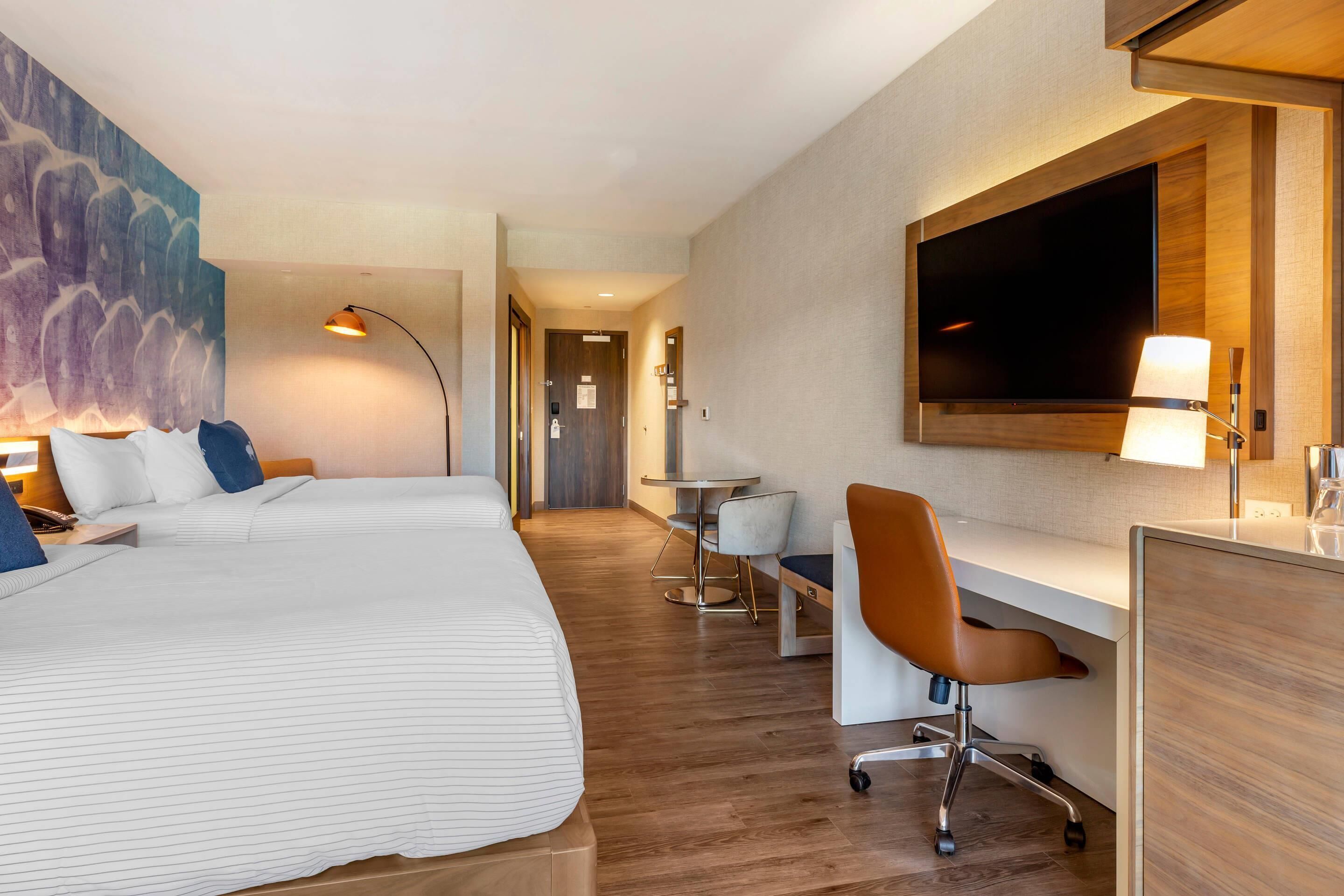 Una camera d'albergo con un letto, una scrivania, una sedia, TV e un quadro appeso al muro.