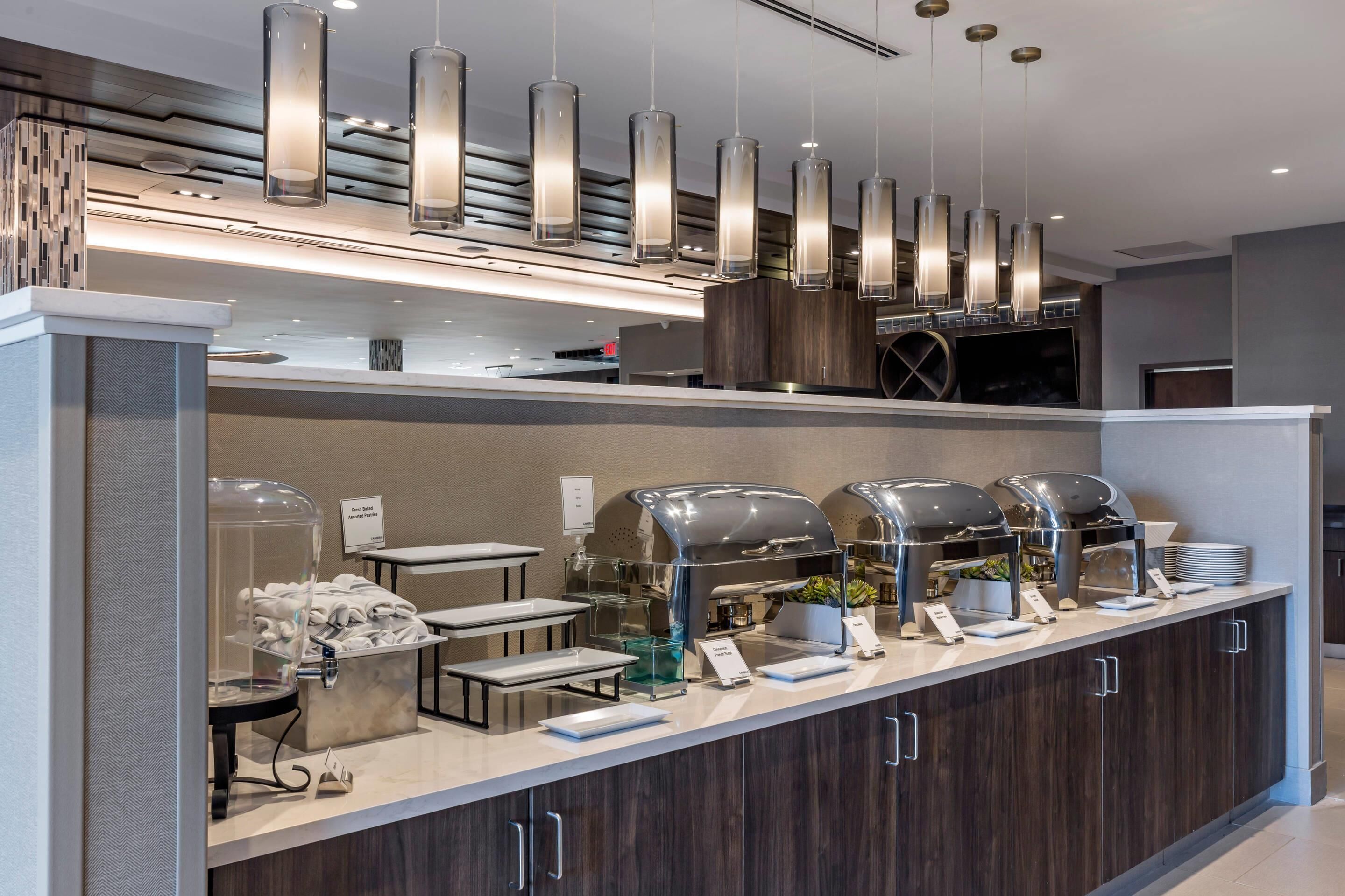 Ein Buffet mit transparenten Glasabdeckungen, eine Kaffeestation und eine moderne Pendelleuchte.