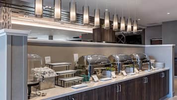 A buffet setup with clear glass covers, a coffee station, and a modern pendant light fixture.