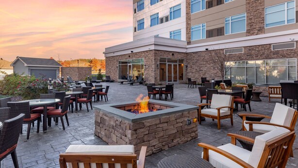 Un patio de hotel con mobiliario exterior, una chimenea y un edificio de varios pisos con grandes ventanales.