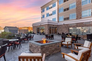 A hotel patio with outdoor seating, a fire pit, and a building with multiple floors and large windows. - Cambria Hotel Manchester South Windsor (South Windsor)