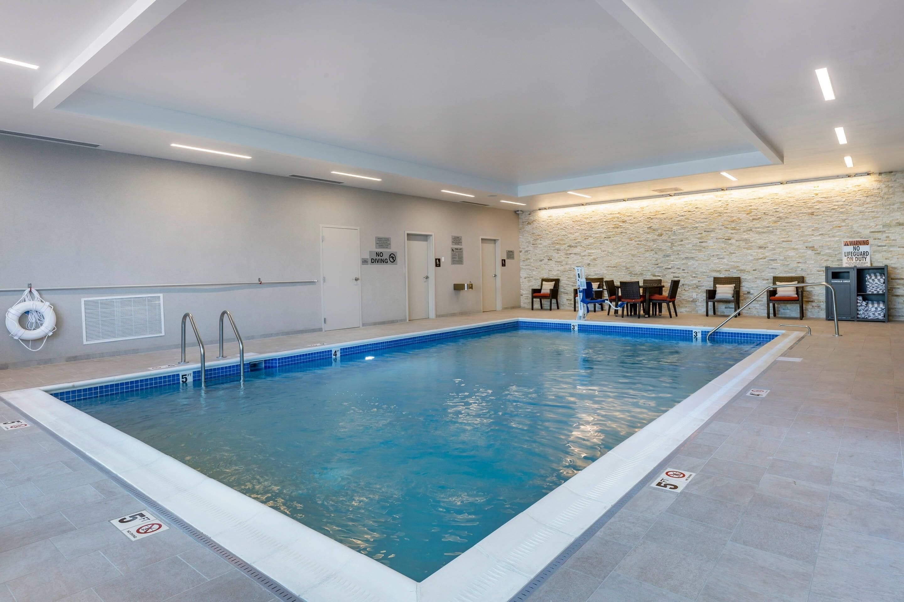 Ein Hallenbad mit klarem Wasser, einer Rettungswache und einer Steinsäule im Hintergrund.