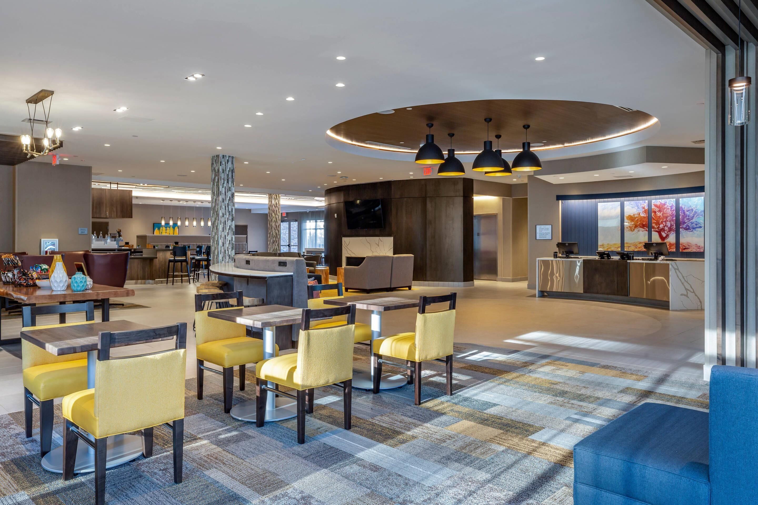 A modern hotel lobby with a reception desk, seating area, and a large window with a view.
