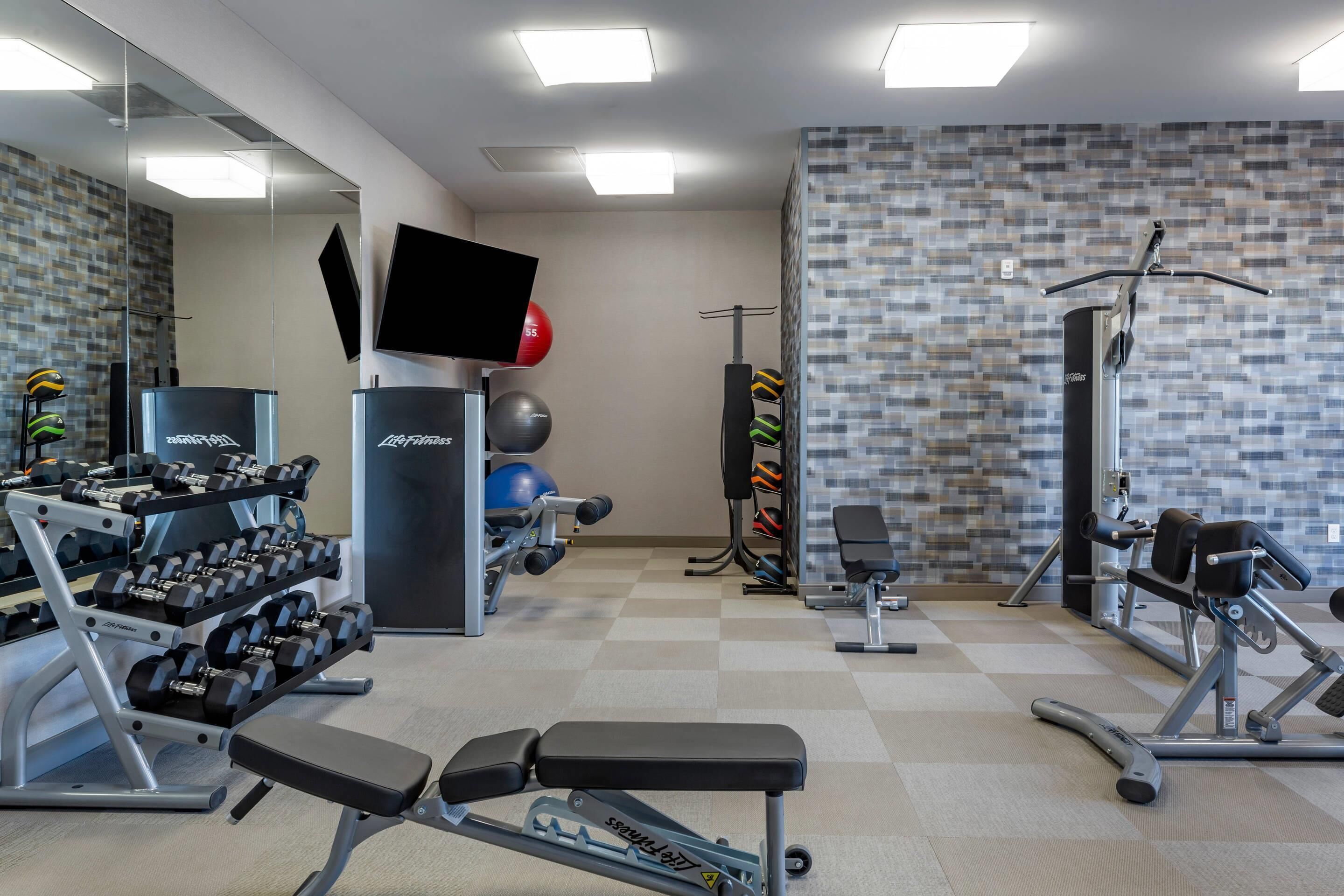 Un gimnasio con equipo de levantamiento de pesas, pelotas de ejercicio y una televisión.