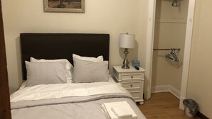 A neatly made bed with white linens, a bedside lamp, and a small bedside table with a remote control and a box. - Walk to Wrigley Field/Monthly Discounts Available (Chicago)