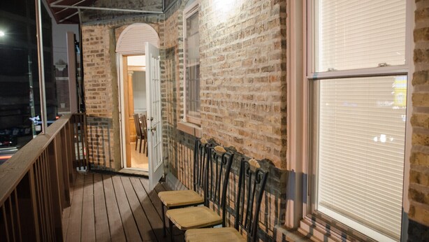 A wooden deck with chairs, a brick wall, and a window with blinds. - Walk to Wrigley Field/Monthly Discounts Available (Chicago)
