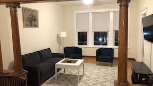 A living room with a dark-colored sofa, two armchairs, a coffee table, a patterned rug, and a painting on the wall. - Walk to Wrigley Field/Monthly Discounts Available (Chicago)