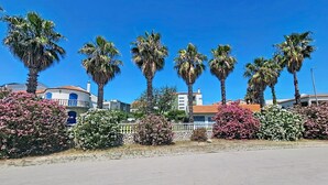 Calle con palmeras y arbustos floreados, edificios con tejados de tejas rojas y un cielo azul despejado.