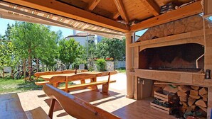 Un patio al aire libre con chimenea de piedra, bancos de madera y una pérgola.