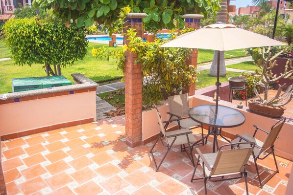 A patio with a table and chairs, surrounded by a brick wall, a pool, and greenery.