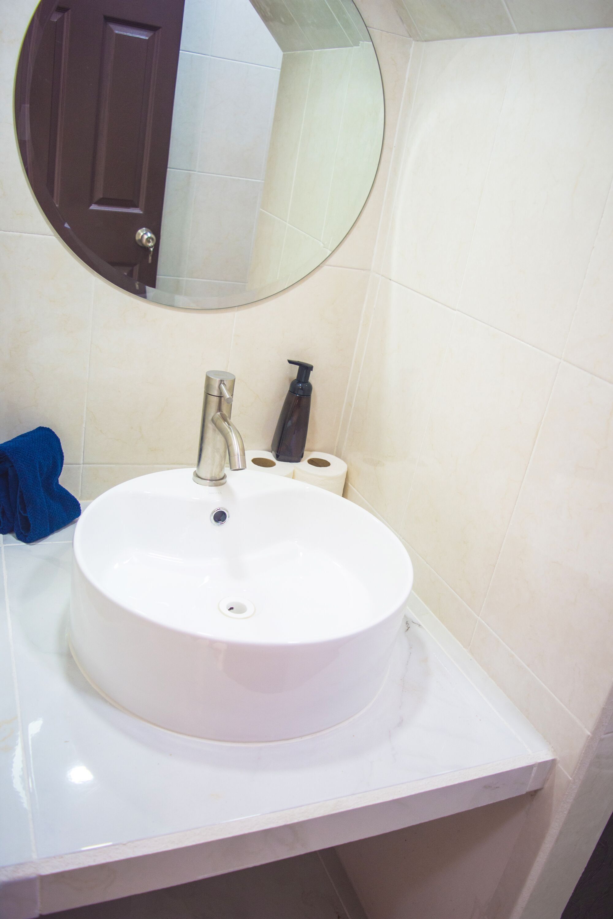 A bathroom with a white sink, a mirror, a towel, and a toilet paper roll.
