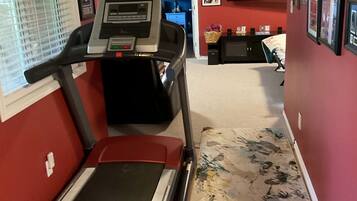 A home gym with a treadmill, a small desk, and a chair.
