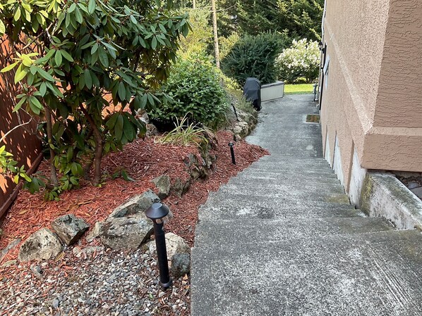 A pathway leading to a building with a stone wall on one side and a garden with mulch and rocks on the other.