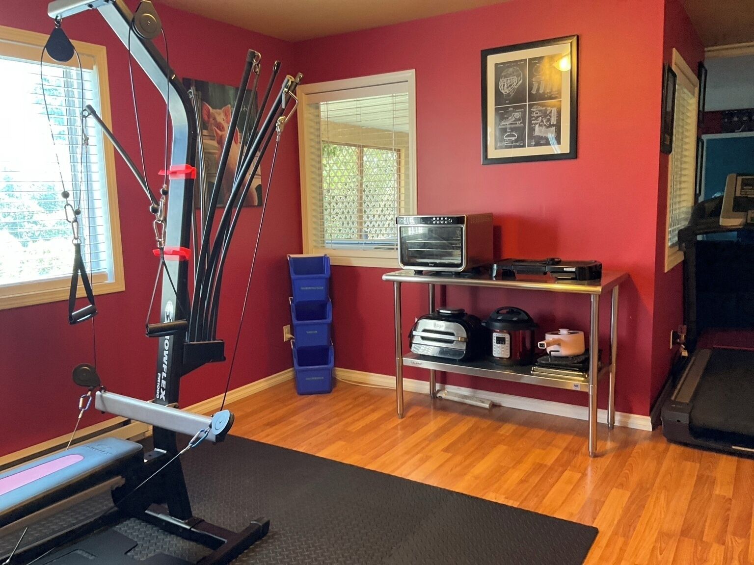 Un gimnasio en casa con equipo de ejercicio, una cinta de correr y una ventana con persianas.