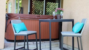 Un jacuzzi con tapa de madera, dos sillas con cojines turquesa y una mesa con dos copas de vino y una planta en maceta.
