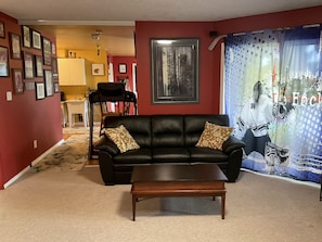 A living room with a black leather sofa, a wooden coffee table, and a dining area in the background.