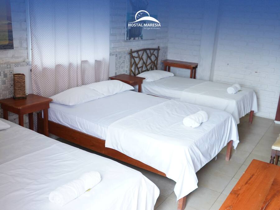 Quarto de hotel com três camas de solteiro, cabeceiras de madeira e uma pequena mesa de madeira.