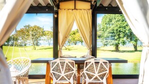 Un comedor con una mesa y sillas, un sillón colgante y vistas a un lago y árboles.