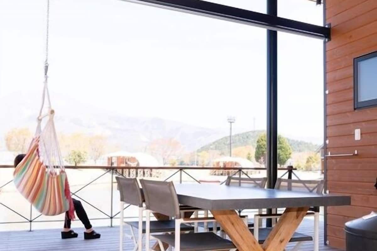 A wooden deck with a table and chairs, a hanging chair, and a view of the outdoors.