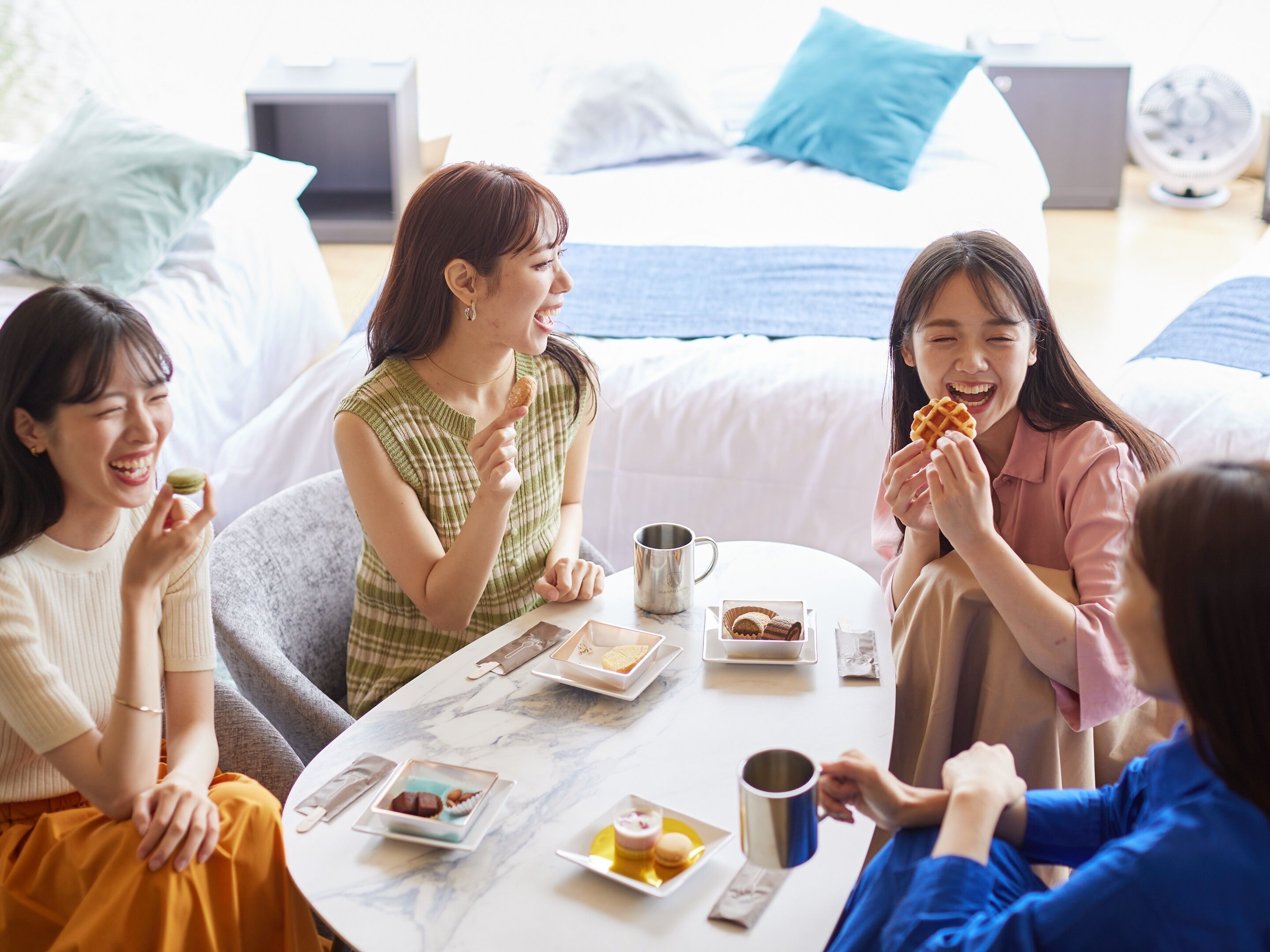 A group of people sitting around a table in a room with a bed and pillows in the background.