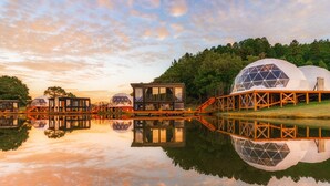 Un resort junto al lago con alojamientos en cúpulas geodésicas, pasarelas de madera y reflejos en el agua.