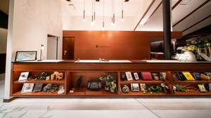 Un mostrador de recepción con detalles de madera, un cartel en la pared que dice "GLAMP ELEMENT" y estanterías debajo que exhiben obras de arte enmarcadas, libros y objetos decorativos.