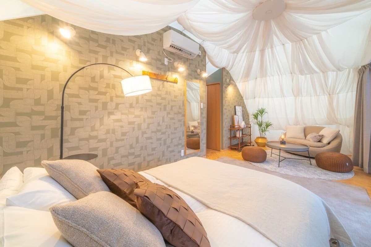 A modern bedroom with a large bed, a floor lamp, a sofa, and a dining table.