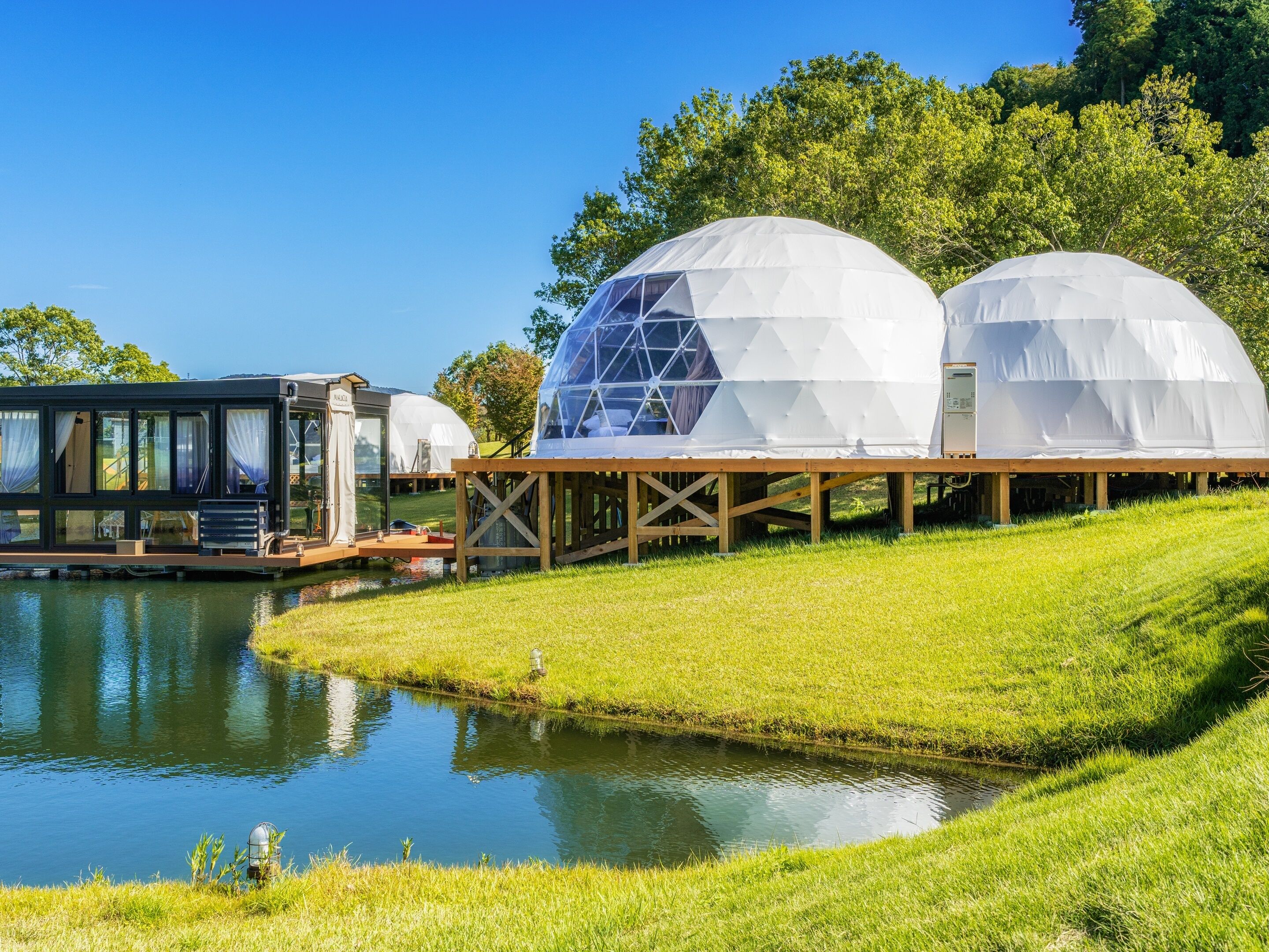 A lakeside property with a glass house and two dome-shaped structures.