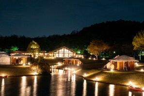 A lakeside resort with multiple tents and a wooden lodge, surrounded by trees and illuminated by night lights. - Glamp Element - Campground (Maibara)