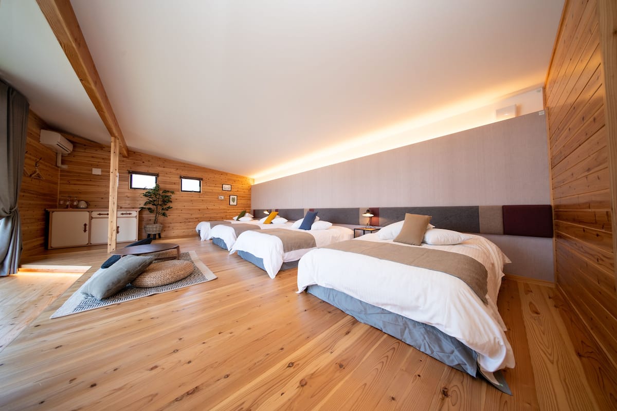 A room with three beds, wooden floors, and a sloped ceiling.