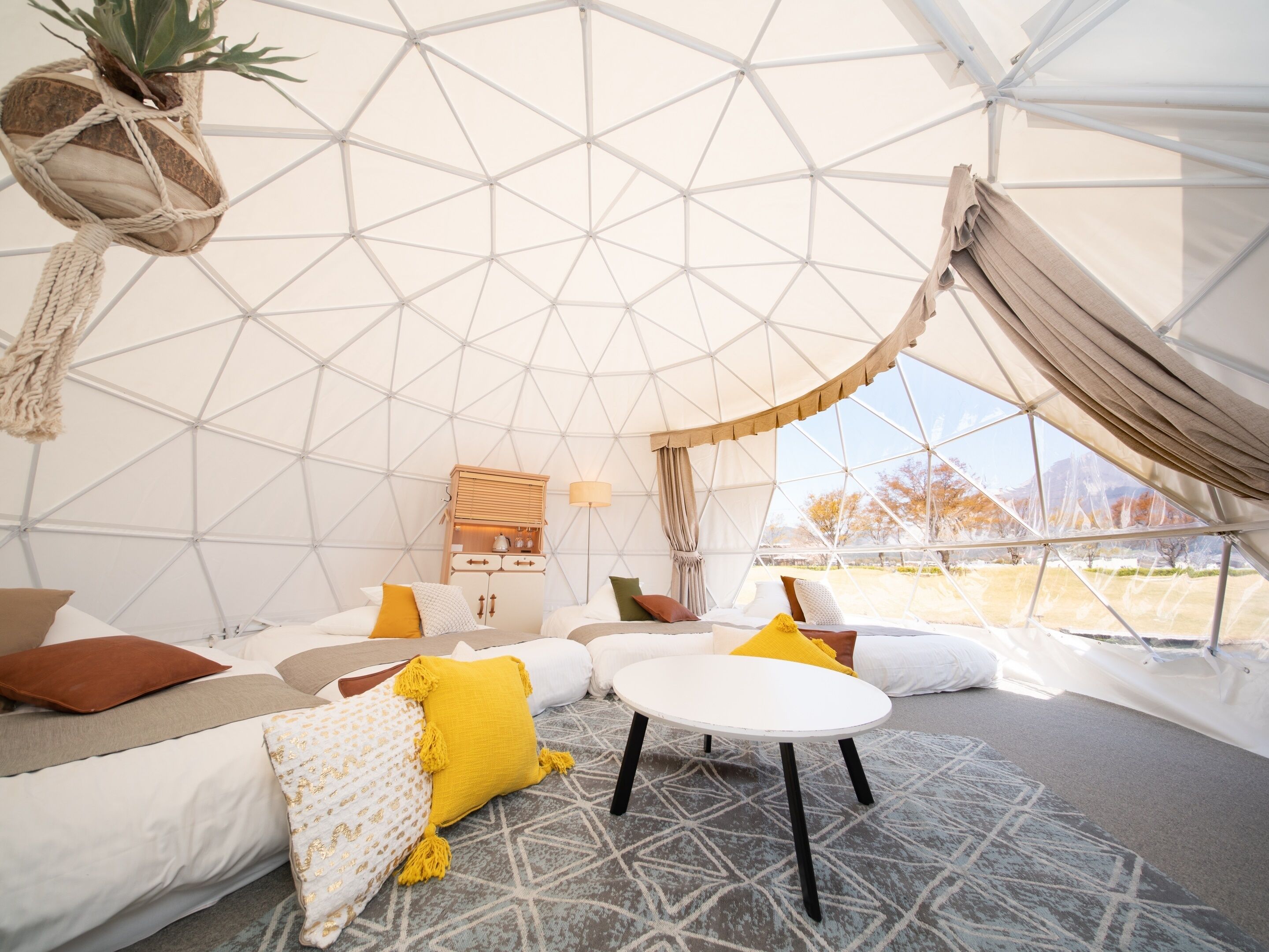 A cozy interior of a geodesic dome with a bed, a small table, and a cabinet.