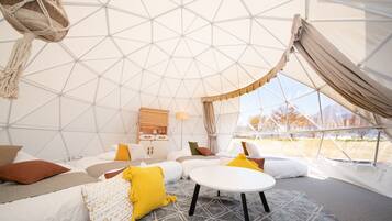 A cozy interior of a geodesic dome with a bed, a small table, and a cabinet.