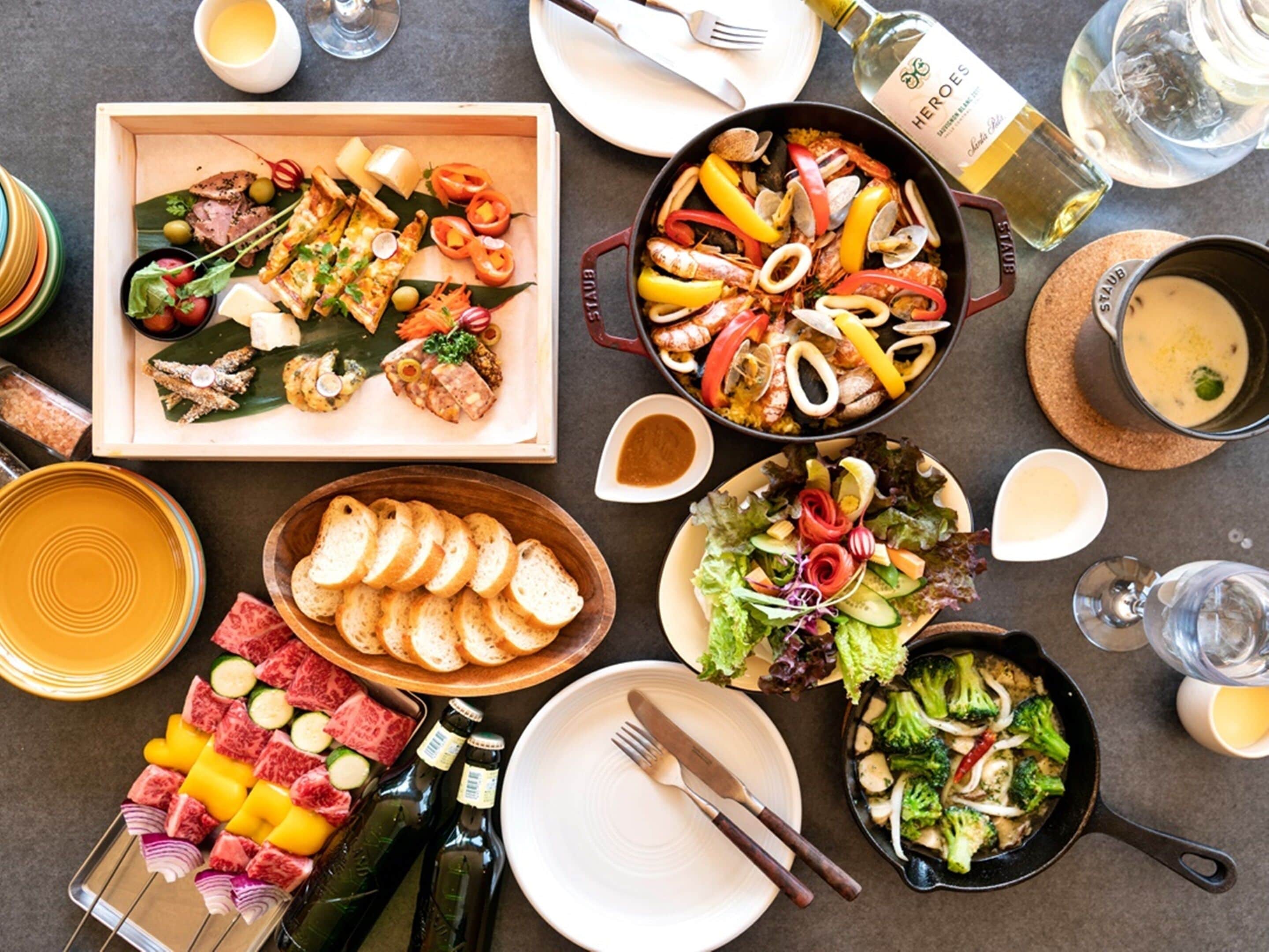 A variety of dishes including seafood, bread, and a salad, arranged on a table with bottles and glasses.
