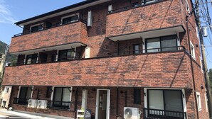 A multi-story brick building with balconies, air conditioning units, and a sign indicating a restaurant. - Condominium MIRAHAKONE (Hakone)
