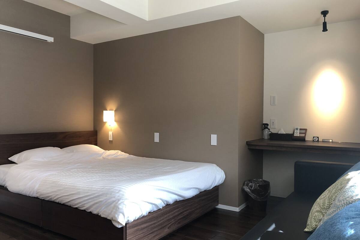 Ein modernes Hotelzimmer mit einem großen Bett, einem kleinen Schreibtisch, einer Wandleuchte und einem Deckenventilator.