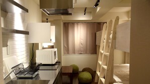 A compact kitchen with a sink, stove, and microwave. There are two green ottomans and a window with curtains. - Condominium MIRAHAKONE (Hakone)
