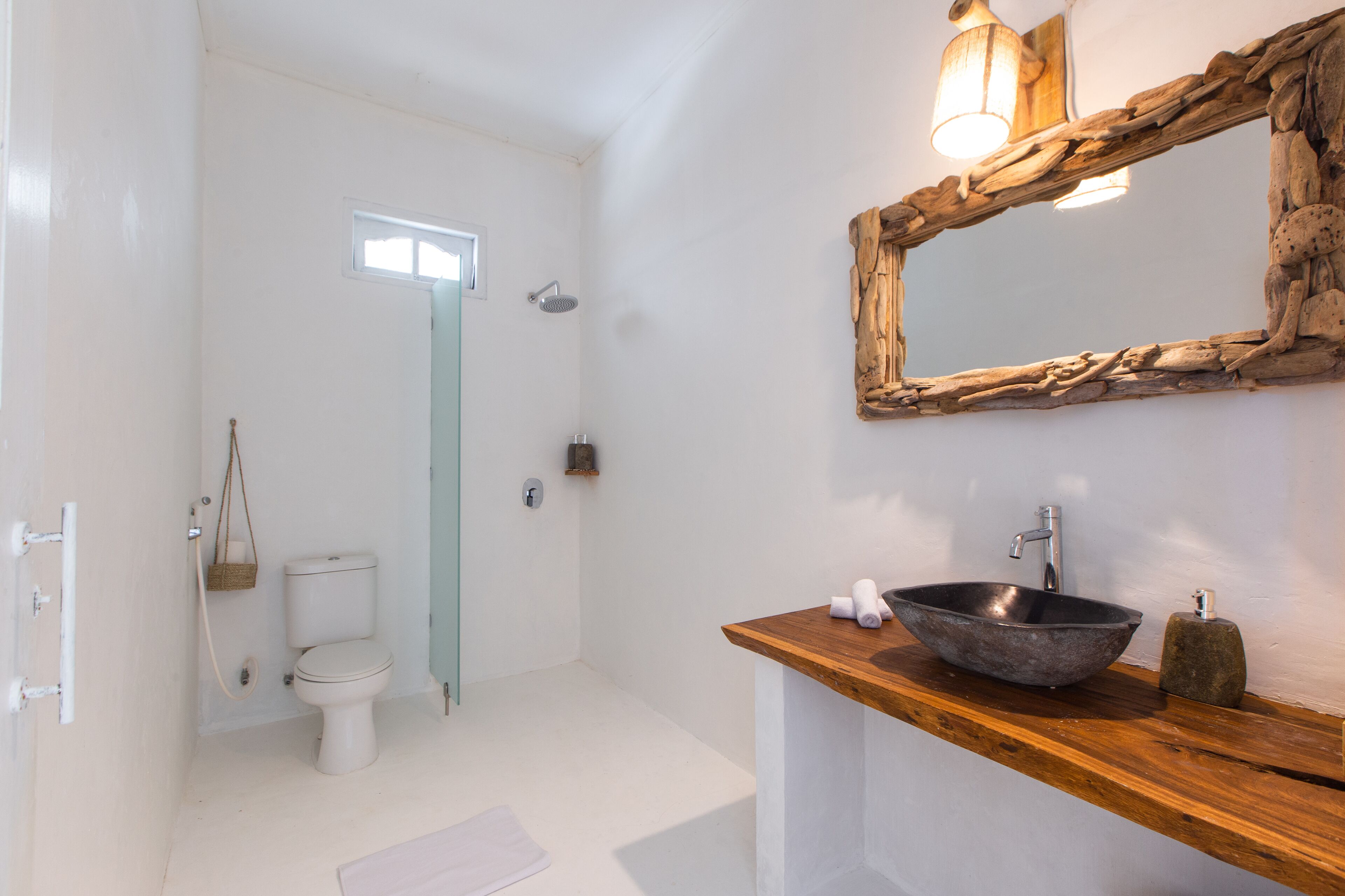 A bathroom with a white toilet, a wooden vanity with a bowl sink, a mirror, and a shower.