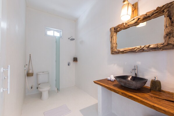 A bathroom with a white toilet, a wooden vanity with a bowl sink, a mirror, and a shower.