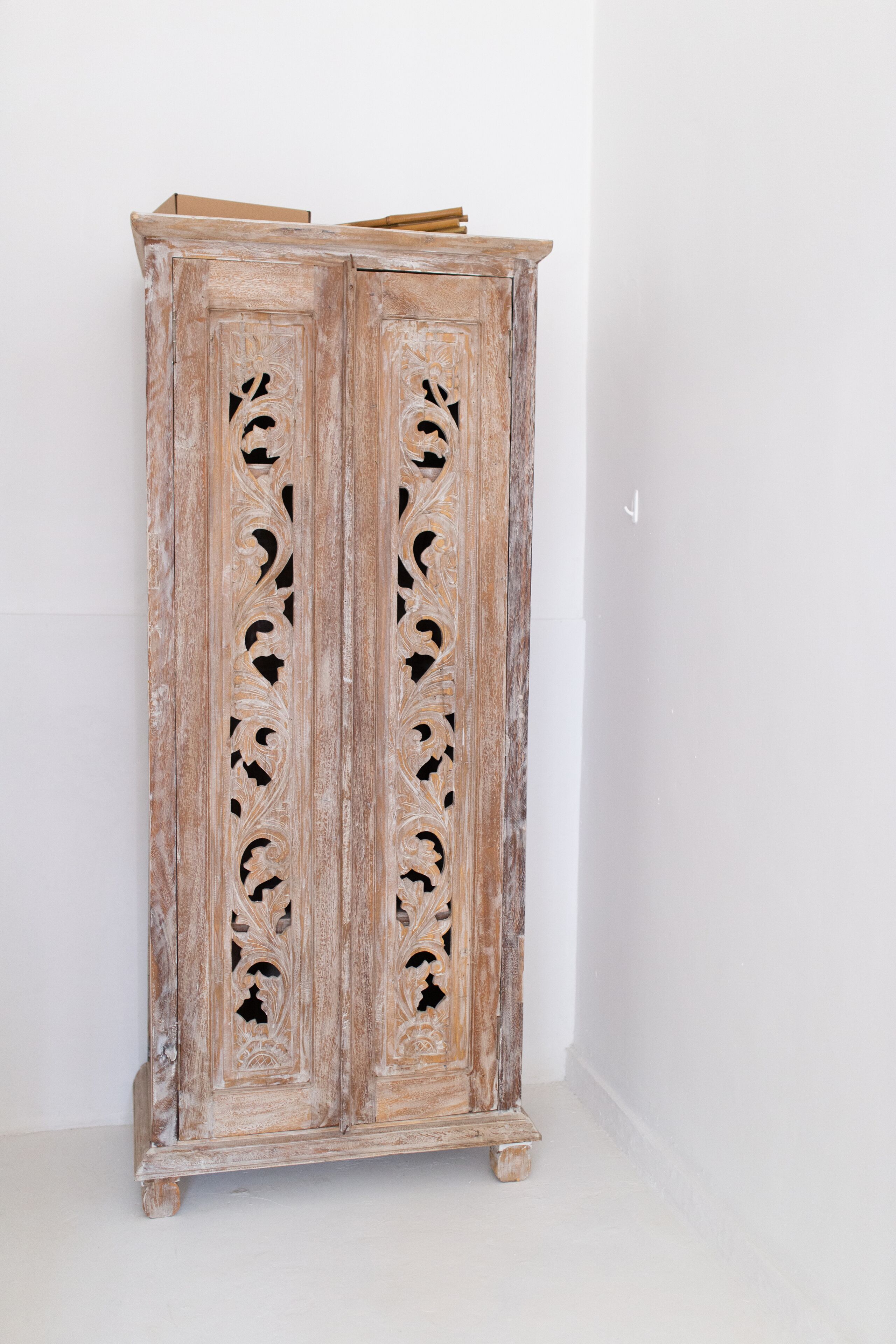 A tall, rustic wooden cabinet with intricate carvings and a flat top shelf.