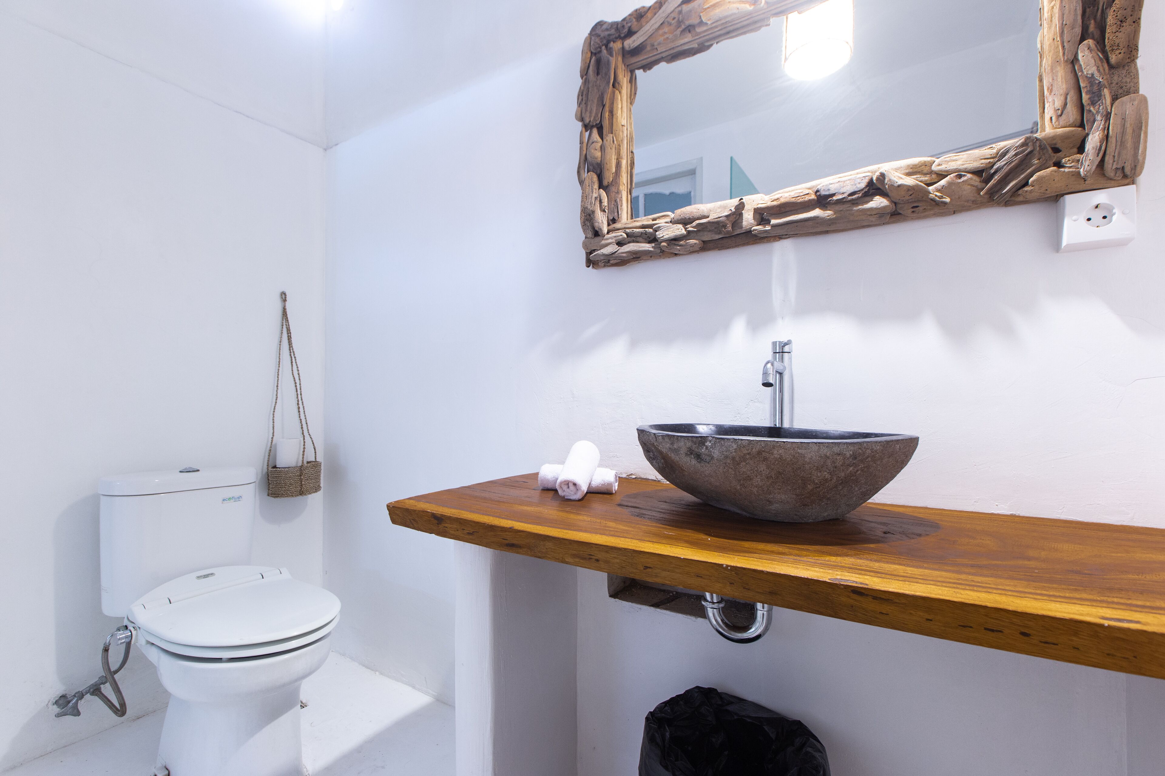 A bathroom with a white toilet, a wooden vanity with a stone sink, and a rustic mirror.