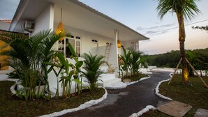 Une maison blanche avec un porche, entourée de plantes tropicales et d’un palmier.