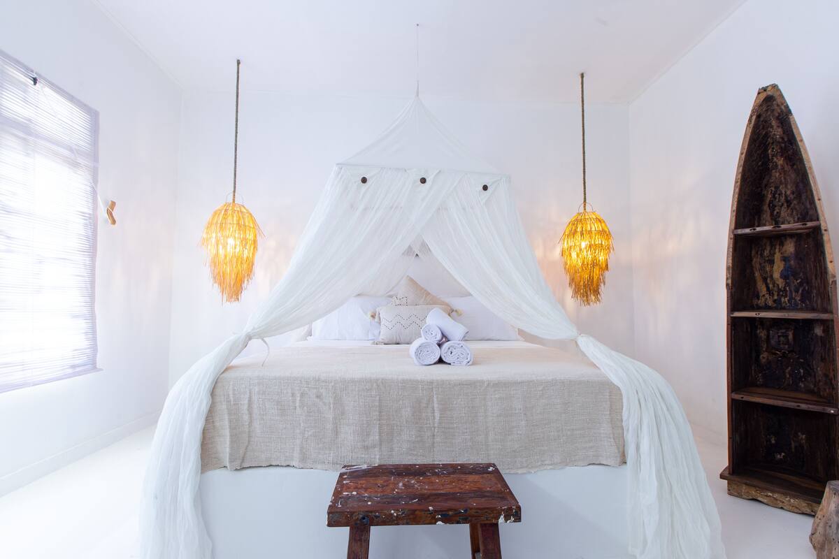 Een bed met baldakijn, twee hanglampen, een houten bank en een rustieke boekenkast.