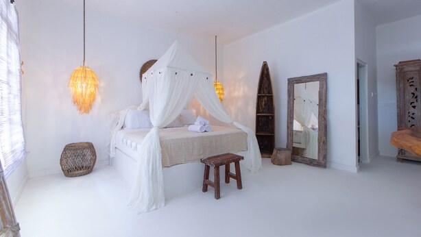 Une chambre à coucher avec un lit à baldaquin, un petit tabouret en bois, un panier en osier et un miroir au mur.