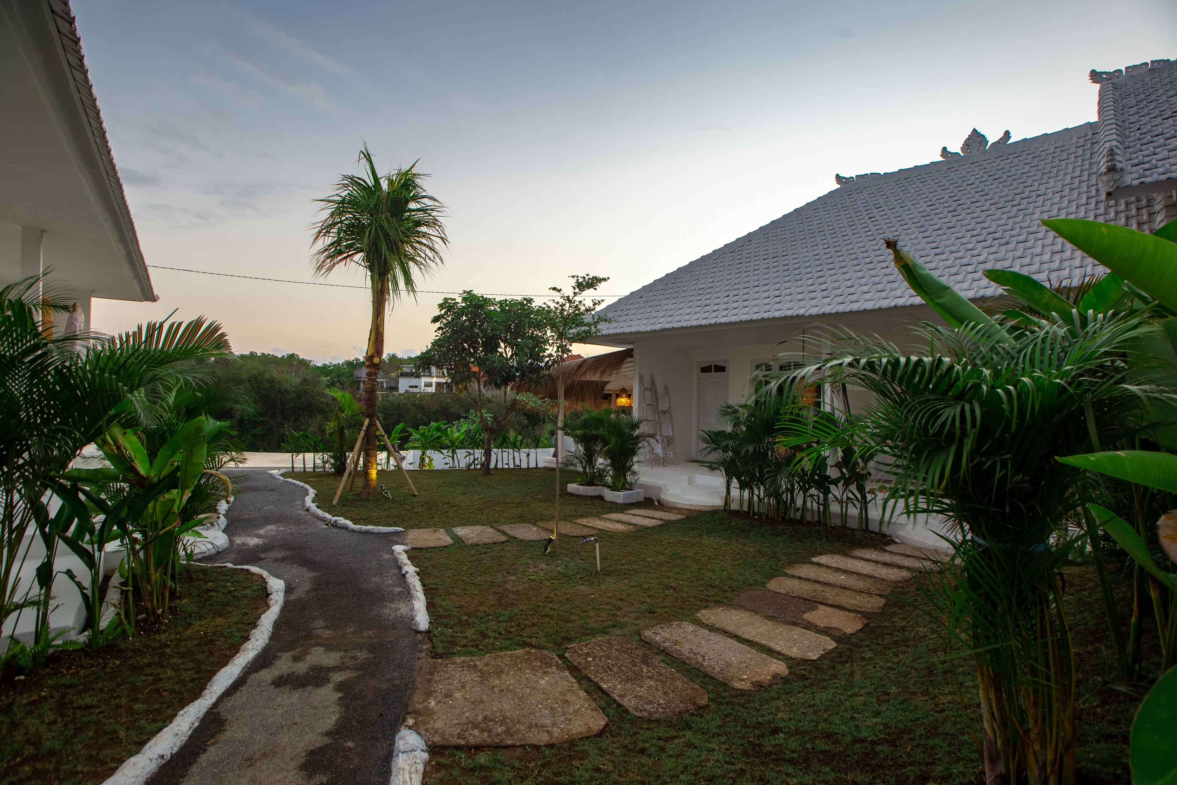 Uma trilha leva a uma casa com telhado de telhas, cercada por vegetação e um pequeno jardim.