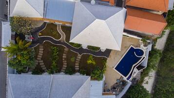 Vista aérea de un barrio residencial con varias casas, una piscina y un jardín con palmeras.