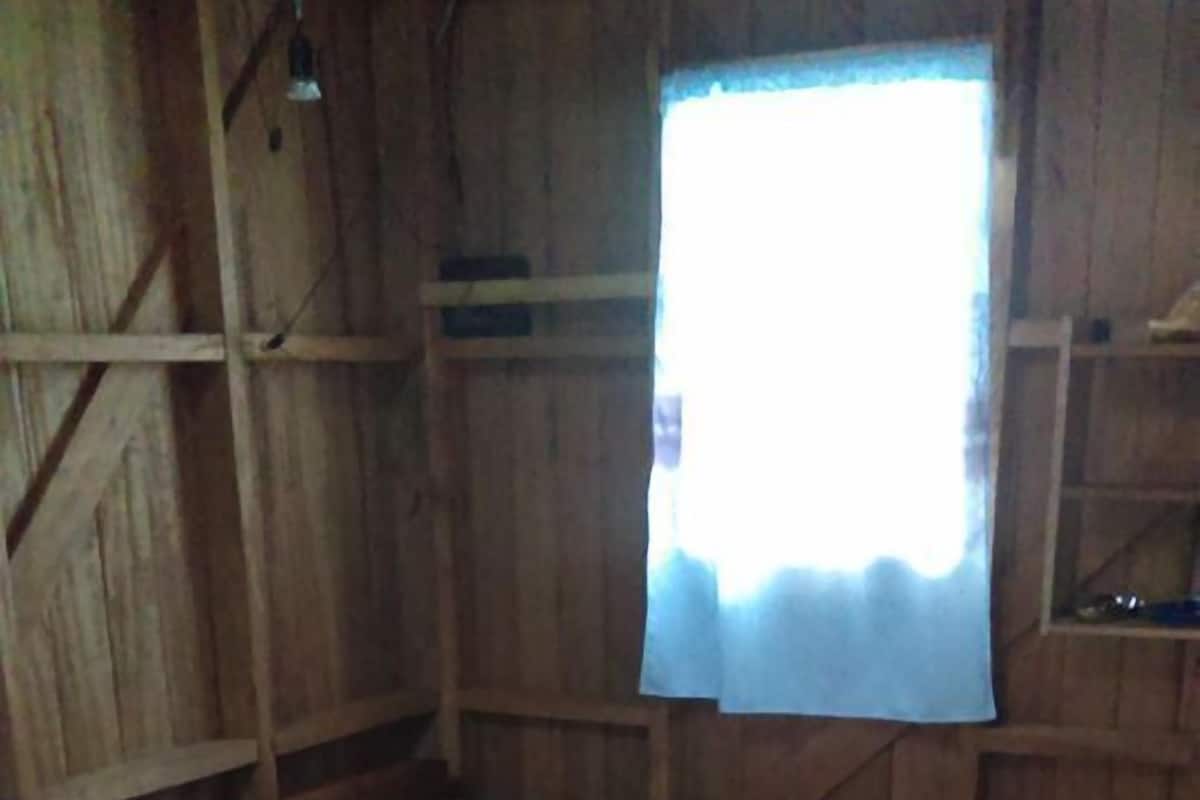 Two wooden beds with white linens and a window with a white curtain.