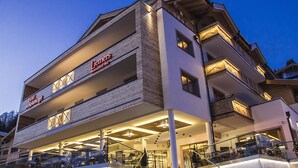 Un hotel de varios pisos con un restaurante en la planta baja, que presenta un diseño arquitectónico moderno con balcones y una entrada bien iluminada.