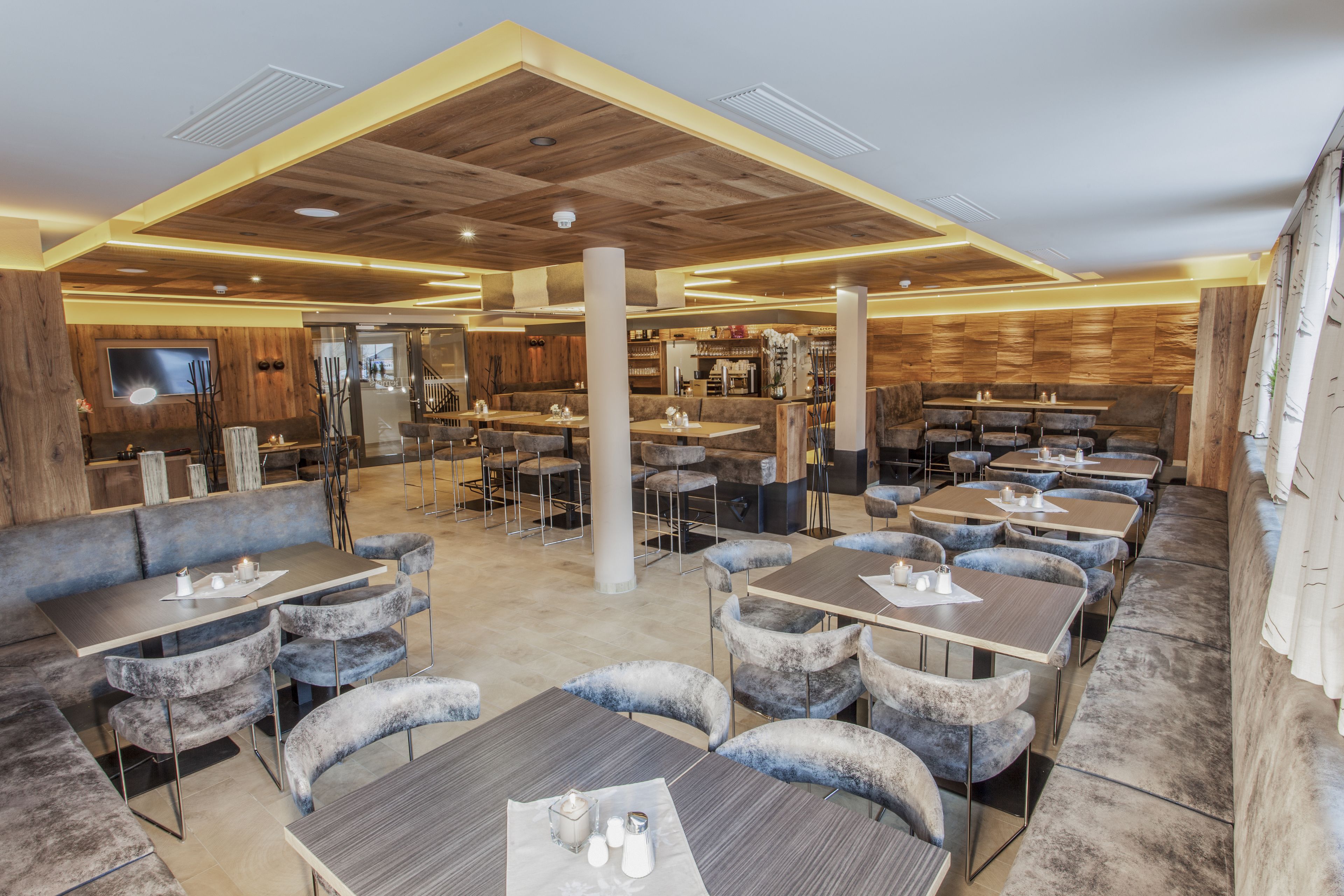 A spacious restaurant with multiple seating areas, including booths and tables, and a wooden ceiling design.