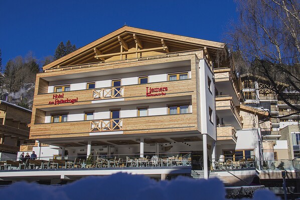 Un hotel con fachada de madera, varios balcones y una terraza con mobiliario exterior.